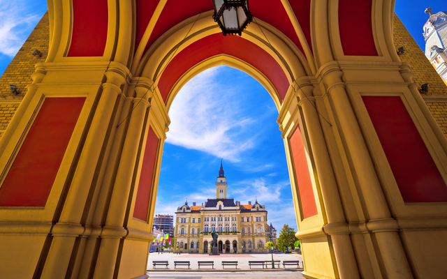 Blick durch einen Bogen auf ein historisches Gebäude mit Turm bei sonnigem Himmel.