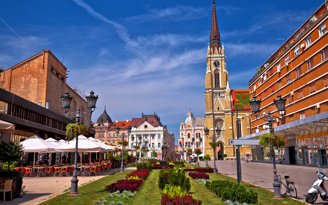 Platz mit historischen Gebäuden und einer Kirche im Hintergrund bei blauem Himmel.