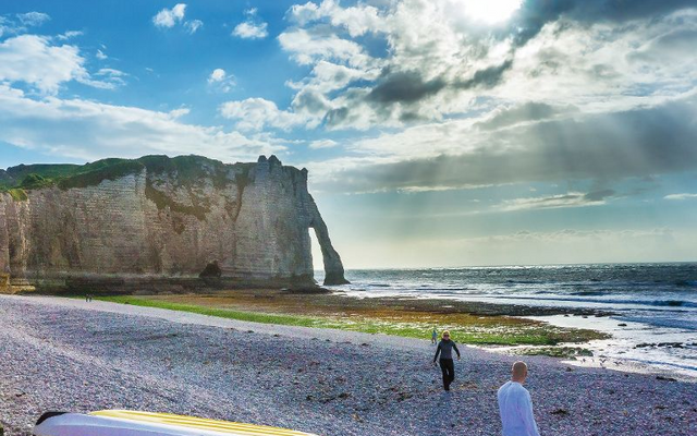 Felsen am Meer bei sonnigem Wetter mit ein paar Menschen am Strand und Booten im Vordergrund.