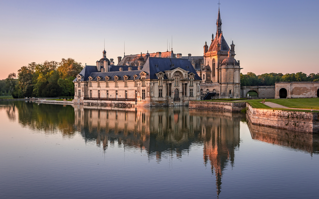 Schloss mit spiegelndem Wasser im Sonnenuntergang.