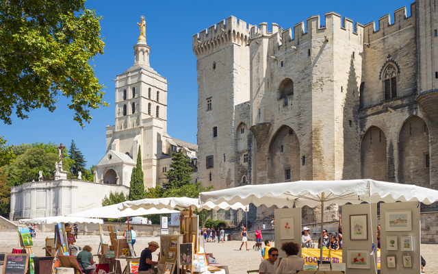 Menschen besuchen Kunstausstellung vor Papstpalast in Avignon bei Sonnenschein.